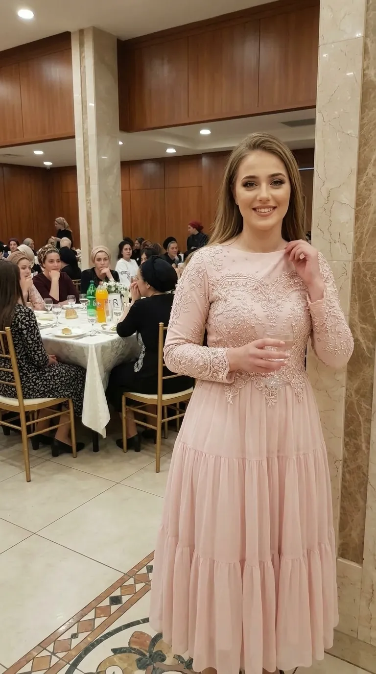 שמלת ערב בצבע ורוד פודרה הכוללת צווארון עגול גבוה וחלק עליון צמוד המעוטר ברקמת תחרה עשירה ובחרוזים עדינים. לשמלה שרוולים ארוכים צמודים המכוסים בתחרה תואמת וחצאית שיפון ארוכה ונשפכת המעוצבת בגזרה מדורגת של שלוש קומות.